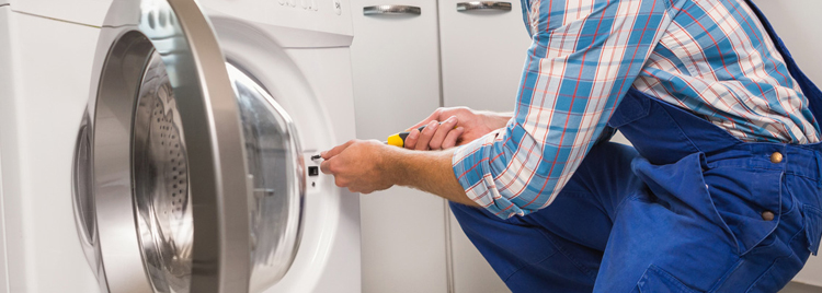 An appliance technician in blue overalls repairing a dryer