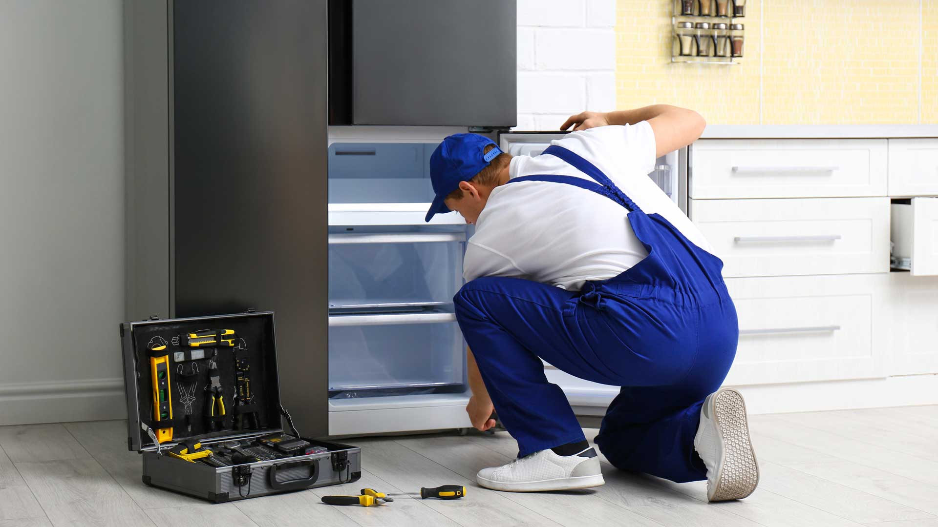An appliance repair man kneeling to inspect the freezer drawer of a refrigerator